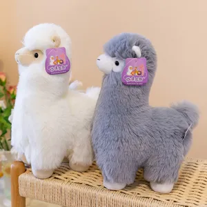 Detailed close-up of cute white and grey alpaca plush toy sitting on a woven stool.