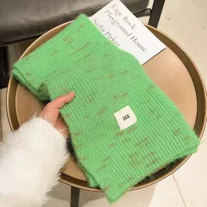Green knitted cashmere scarf with brown monogram pattern and white label for winter.