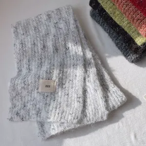 Vista detallada de bufanda de lana tejida acogedora con patrón jaspeado y pequeña etiqueta de marca.