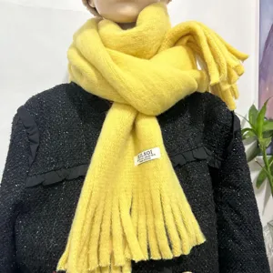 Detail view of a cozy yellow imitation cashmere winter scarf with fringe design and brand tag.