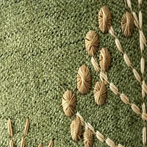 Close-up detail of green chenille fabric with exquisite floral embroidery and French knots.