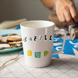 Detail view of a white ceramic coffee mug with letter print placed on a textured table.