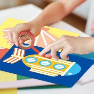 Close-up showing children hands crafting a yellow submarine design with washi tape and cardstock.