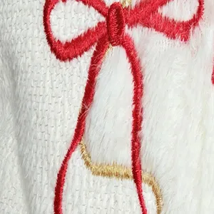 Close-up shot of white plush pillow cover with festive red and gold embroidered bow motif.