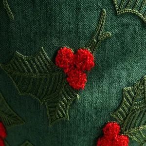 Green plush Christmas pillow cover with embroidered holly leaves and red berries, macro view