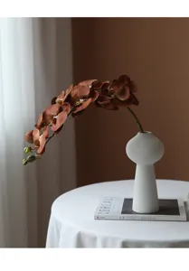 Detail shot of single branch artificial brown phalaenopsis orchid in modern white ceramic vase.