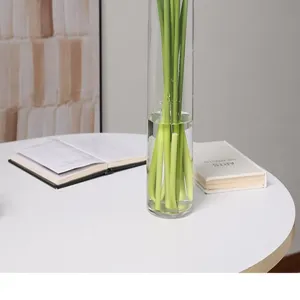 Transparante glazen vaas met groene kunstbloemstelen voor moderne huisdecoratie.