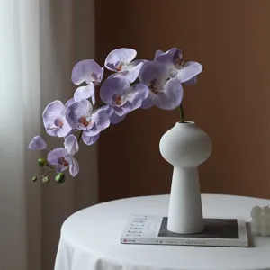 Artificial purple orchid flower branch in white ceramic vase for home table decor elegance