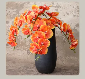 Gedetailleerd uitzicht op kunstmatige oranje phalaenopsis orchideeën bloemarrangement in zwarte vaas.
