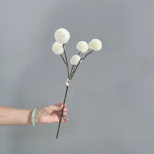 Close up detail of artificial white pompon chrysanthemum flower branch held by hand.