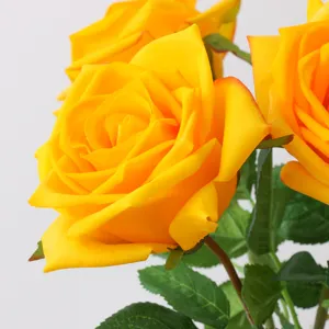 Gedetailleerde close-up van levendige gele kunstmatige rozenbloemen met realistische bladeren.