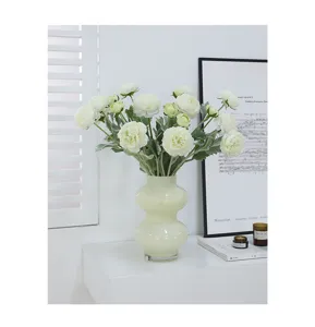 Detailed view of an elegant artificial ranunculus flower bouquet in a modern glass vase.