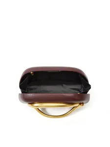 Detail view of burgundy hard-shell box clutch with unique metallic gold sculptural handle.