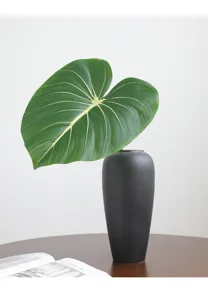Close-up of artificial philodendron leaf in matte black vase, stylish home decor plant.