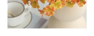 Delicate artificial plum blossom detail, close-up view of orange faux flowers in white vase.