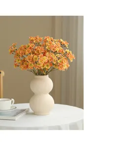 Detailed view of artificial orange flower bouquet in white ceramic vase on clean table setup.