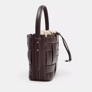 Gros plan détaillé du sac seau en cuir tressé marron foncé avec coutures contrastées.