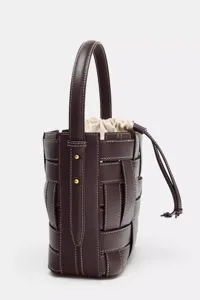 Gros-plan du sac-seau tressé en cuir marron foncé avec poignée et coutures contrastées.