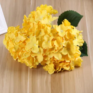 Primo piano di fiori di ortensia di seta gialla artificiale con foglie verdi per la casa.