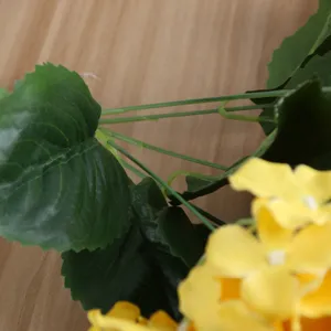 Dettaglio in primo piano di fiori di ortensia gialli artificiali e foglie sul legno.