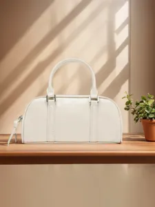 Detailansicht der weißen Leder Boston Tasche auf Holztisch mit eleganter Beleuchtung und Pflanze.