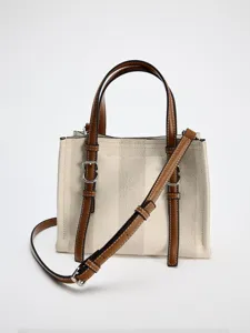 Vista detallada del elegante bolso cruzado de lona beige con detalles de cuero marron.