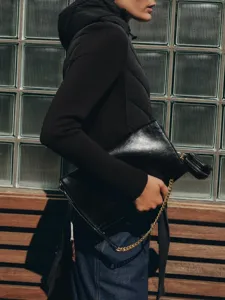 Black shiny leather shoulder bag detail featuring a stylish gold chain and mini pouch.