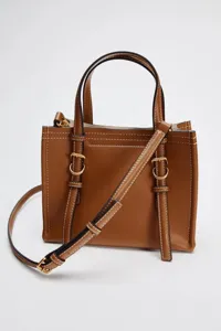 Détail de mini sac bandoulière en cuir marron, montrant coutures et boucles dorées.