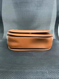 Detailed view of brown leather saddle bag, showing fine stitching and magnetic buckle closure.