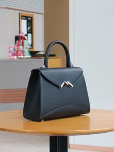 Schwarze Ledertasche Detail, eleganter Metall M-Verschluss auf rundem Holztisch platziert.