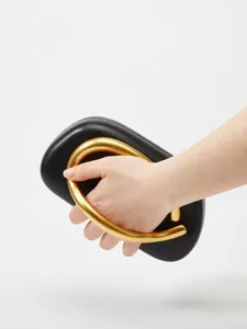 Close-up detail view of the black hard-shell clutch featuring a unique gold ring handle.