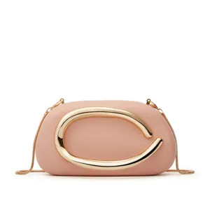Closeup detail of pink leather mini crossbody bag featuring a large gold metallic C-shape handle.