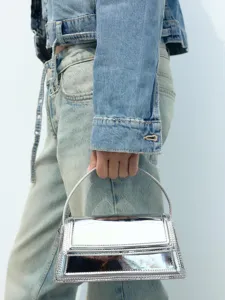 Metallic-silberne Damen-Handtasche mit strukturiertem Griff und stilvollem Jeans-Outfit.