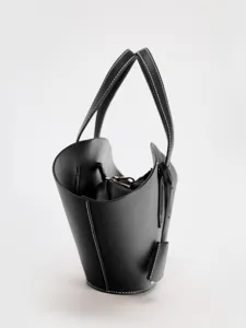 Vue détaillée du sac seau noir minimaliste en cuir avec des coutures contrastées.