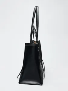 Détail de profil du sac cabas en cuir noir avec surpiqûres blanches et poignées solides.