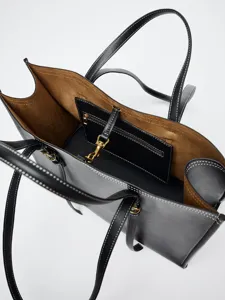 Détail d'un cabas en cuir noir avec surpiqûres contrastées, doublure marron et finitions dorées.