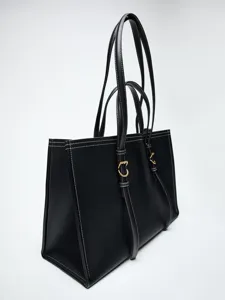 Détail en gros plan du sac fourre-tout noir avec coutures blanches et finitions dorées.