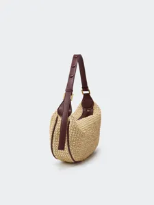 Close-up detail of straw woven shoulder bag featuring brown leather trim and metallic hardware.
