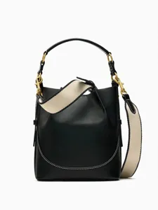 Detailansicht der schwarzen Leder-Eimer-Tasche mit breitem, beigen Gurt und Messingteilen.