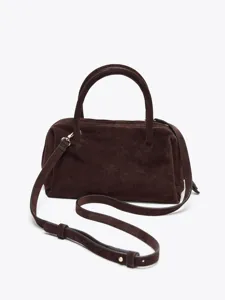 Détail de sac de bowling en daim marron foncé, texture douce et accessoires métalliques fins.