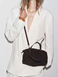 Détail de sac bowling en daim marron foncé, sac à main bandoulière élégant pour femme automne.