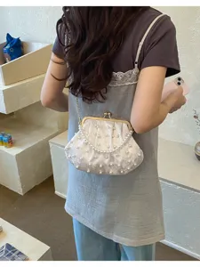 Nahaufnahme der weißen perlenbestickten Bügel-Muscheltasche mit elegantem Metallkettenriemen.