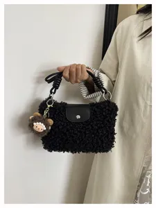 Close-up detail of black fluffy shearling handbag with leather flap and cute plush bear charm.
