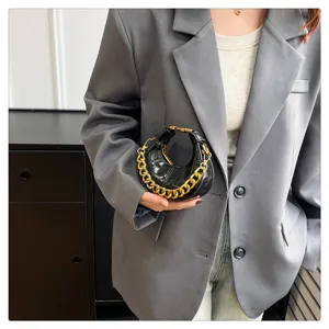 Detailaufnahme einer schwarzen Lackleder-Minihandtasche mit klobigem Goldkettenriemen und Bogen.