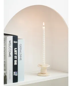 Portacandele in ceramica stile nordico con candela bianca torciata in un accogliente interno.