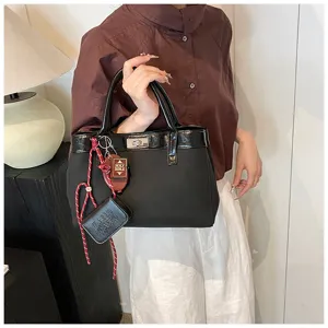 Women's fashion black top handle handbag with stylish turn-lock closure and cute book charm.