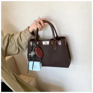 Brown handbag detail view, minimalist style shoulder bag with charming pendants and lock.