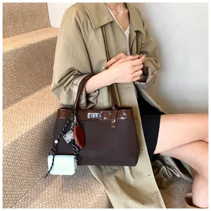 Close-up of the stylish brown handbag featuring trendy charms and structured patent trim.