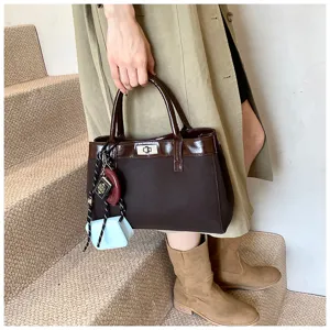 Detail view of stylish brown women tote bag with elegant handle and metallic turn lock closure.