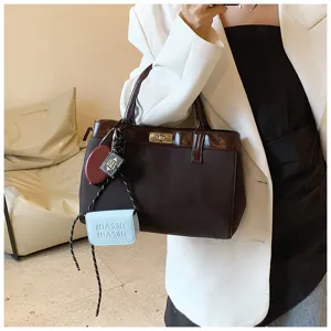 Brown fashion handbag detail showcasing chic turn-lock design and cute mini charm pendants.